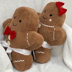 two brown teddy bears sitting next to each other on a white blanket with red bows