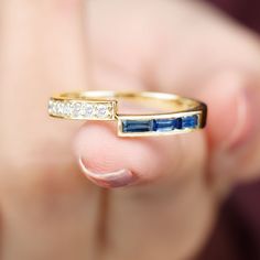 a close up of a person's hand holding a gold ring with blue and white stones