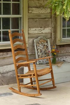 a wooden rocking chair sitting in front of a window next to a planter with flowers