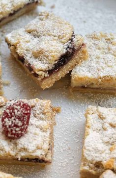 several pieces of dessert on a plate with powdered sugar and raspberry topping