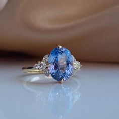 an oval shaped blue and white sapphire ring with three diamonds on the band, set in yellow gold