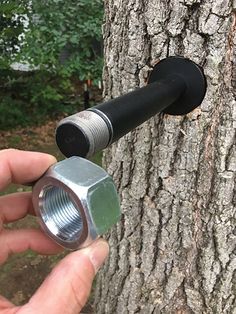 a hand holding a metal nut in front of a tree with a hose attached to it