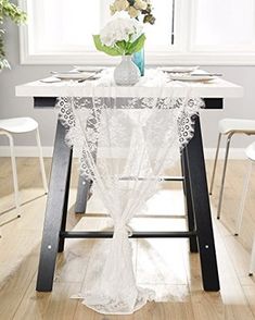 a table with white chairs and flowers in a vase on top of it, next to a window