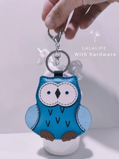 a small blue and white owl keychain is being held by a person's hand