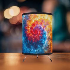 a colorful lamp is sitting on a wooden table with blurry lights in the background