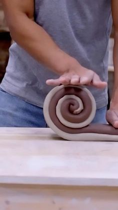 a man is making a spiral cake on top of a wooden table with his hands