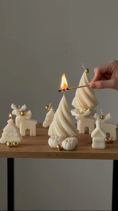 a person lighting a candle in front of small white christmas trees on a wooden table