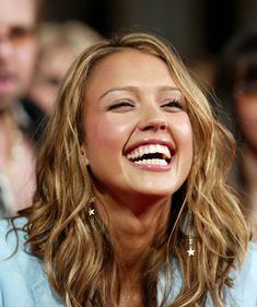 a close up of a smiling woman with long hair and wearing gold hoop earrings on her left ear