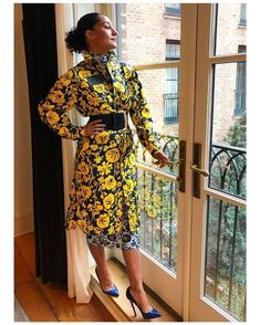 a woman standing in front of a window wearing a yellow and black floral print dress