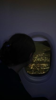 a woman looking out an airplane window at the city lights