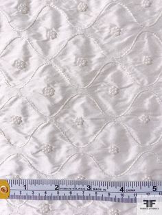 a ruler is measuring the width of a white quilted bed spread with small flowers on it