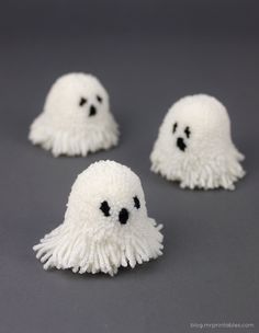 three white pom - poms with black eyes are shown on a gray surface