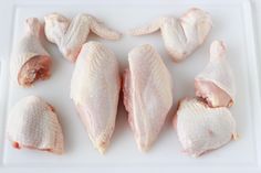 raw chicken wings laid out on a white cutting board with one wing removed from the top