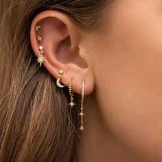 a woman's ear with gold stars and moon earrings on top of her ear