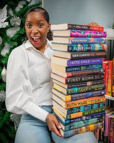 a woman holding a stack of books in front of a christmas tree