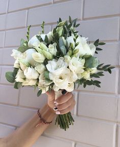 a woman holding a bouquet of white flowers in her left hand against a brick wall