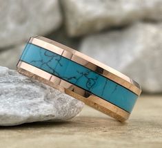 a gold and turquoise ring sitting on top of a rock next to a stone slab