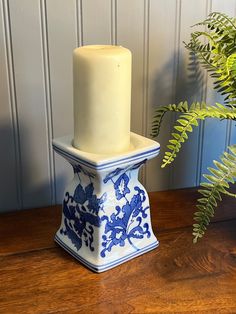 a white candle sitting on top of a blue and white vase next to a plant