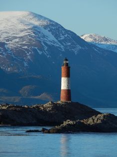 a red and white light house sitting on top of a rock in the middle of water