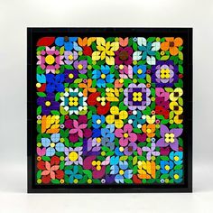 a multicolored square shaped artwork with flowers and leaves on the bottom, in black frame