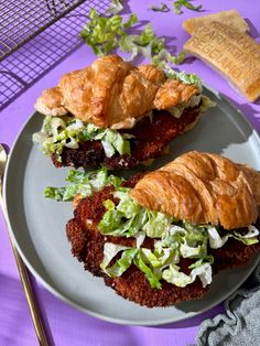 two croissants with lettuce and meat on a plate next to bread