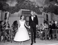 a bride and groom are holding hands in front of an outdoor dining area with people sitting at tables