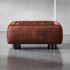 an orange and black checkered ottoman sitting on top of a metal stand in front of a white wall