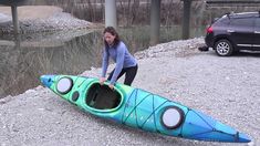 a woman standing next to a blue and green kayak