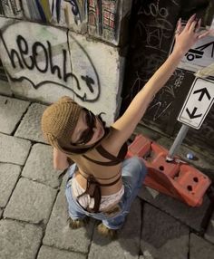 a woman sitting on the ground with her arms in the air next to a street sign