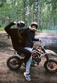 two people on dirt bikes posing for a photo in front of some trees and woods