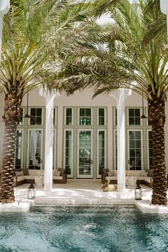 palm trees in front of a house with a swimming pool and lounge chairs around it