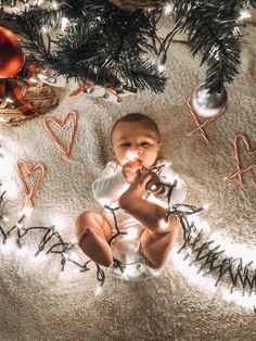 a baby sitting under a christmas tree surrounded by ornaments and lights on the floor in front of it