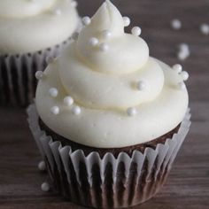 three cupcakes with white frosting and sprinkles on a table