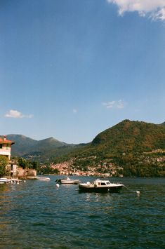 several boats floating on the water in front of a town and mountain range behind them