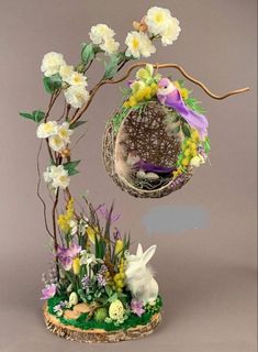 an easter decoration with white flowers and purple birds in a nest on a tree branch