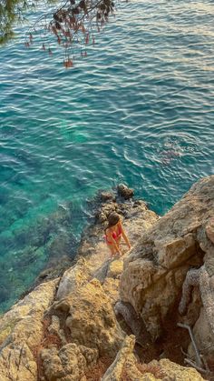 a woman standing on the edge of a cliff next to the ocean with clear blue water