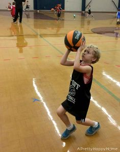 a young boy holding a basketball on top of a hard wood floor in a gym