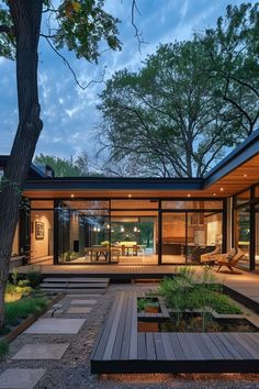 a modern house with wooden decking and glass walls at dusk, surrounded by trees