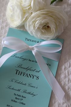 two white flowers on top of a blue and white wedding card with a satin ribbon