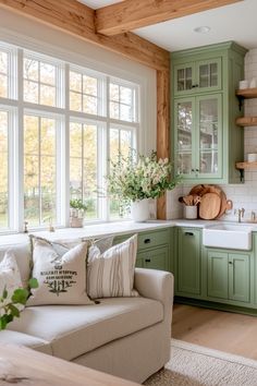 a kitchen with green cabinets and white counter tops, along with a couch in front of the window