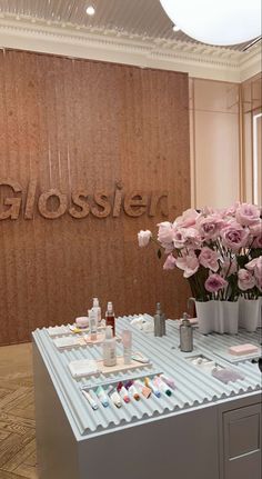 a table with flowers and cosmetics on it in front of a sign that reads glosses