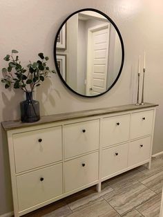 a white dresser sitting next to a mirror and vase with flowers on top of it