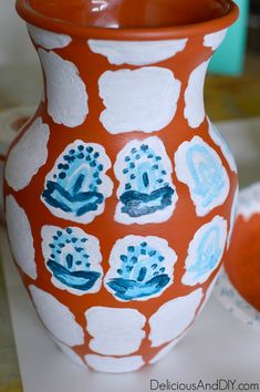 a red and white vase sitting on top of a table next to another orange bowl