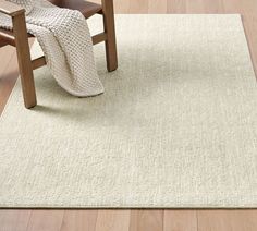 a white rug on the floor with a chair and blanket in front of it next to a wooden table