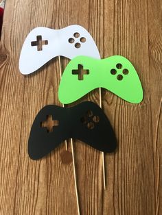 three game controllers on sticks with green and white paper cutouts in the shape of video games