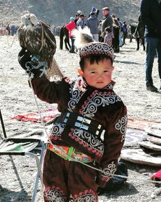 a young boy holding an eagle on his arm in front of other people and mountains