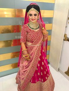 a woman in a red and gold bridal outfit with jewelry on her head, standing next to a wall