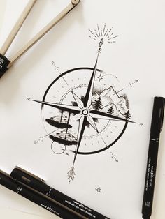 a pen and ink drawing of a compass on paper with mountains in the background next to it