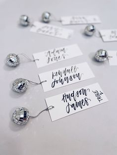 some silver and white tags with names on them sitting on a table next to each other