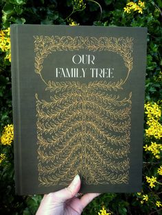 a hand holding up a book with the title our family tree on it in front of some yellow flowers